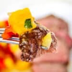 Close-up of a fork holding a piece of beef with colorful bell peppers, with a blurred background.
