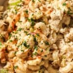 Close-up of a creamy macaroni salad with tuna and a sprinkle of paprika and chopped parsley in a white bowl.