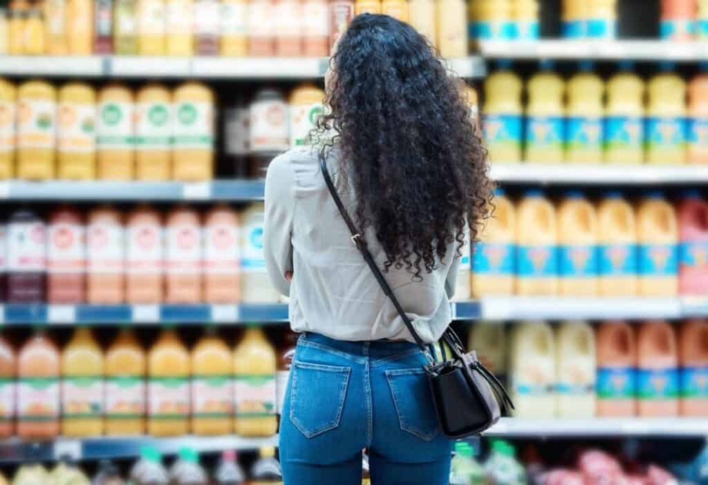 Woman with curly hair shopping for groceries in a supermarket aisle.
