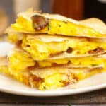 A stack of breakfast quesadillas with scrambled eggs, cheese, and bacon on a white plate.