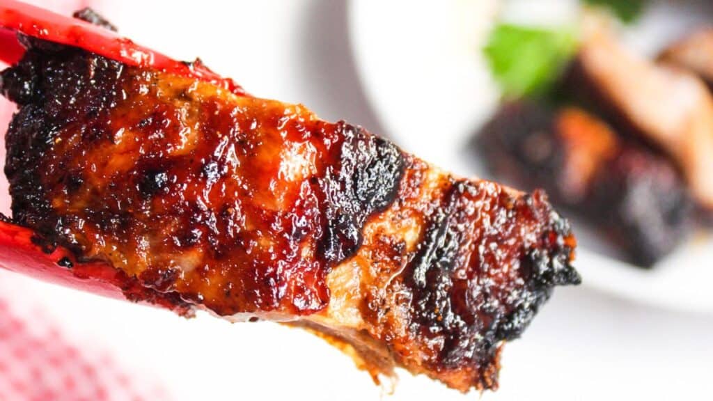 Close-up of an air-fried barbecued rib with charred edges over a white plate.