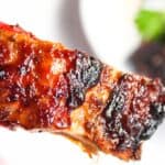 Close-up of an air-fried barbecued rib with charred edges over a white plate.