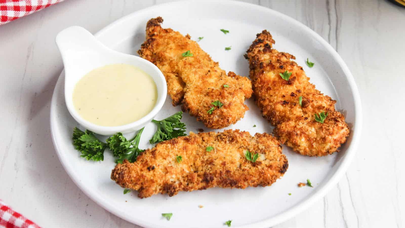 Fried chicken tenders on a plate with dipping sauce.
