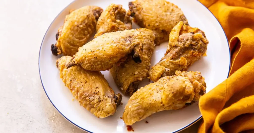 A plate of roasted chicken wings on a white plate with a yellow napkin on the side.