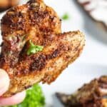 A person holds a seasoned, air-fried chicken wing garnished with parsley.