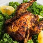 Air-fried Cornish hen served on a bed of kale garnished with lemon wedges.