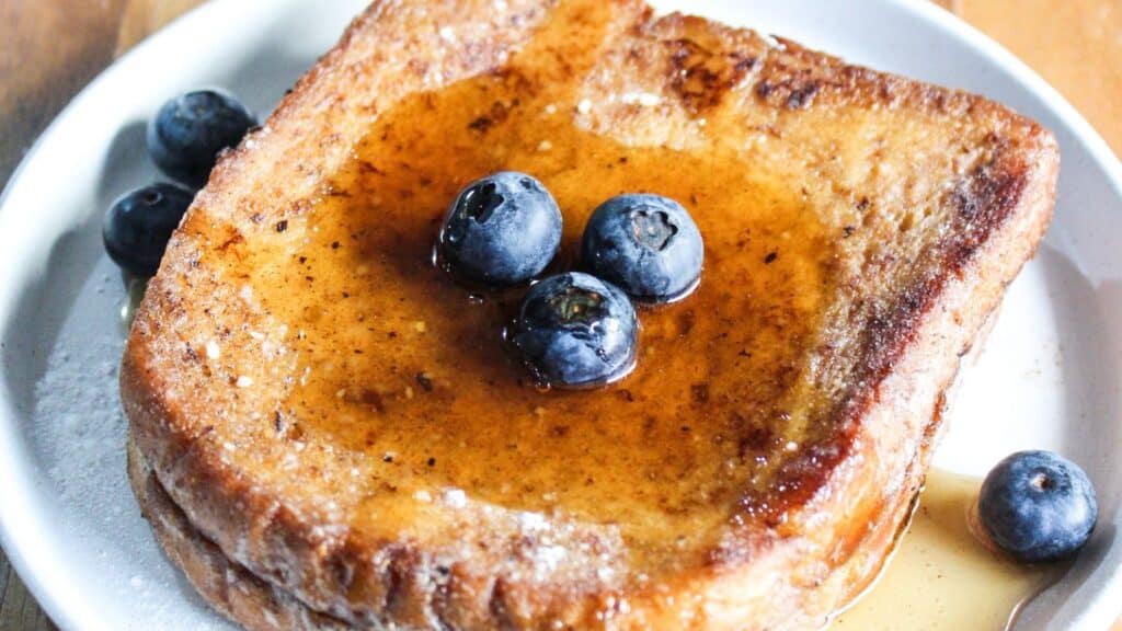 A slice of french toast topped with blueberries and drizzled with syrup.