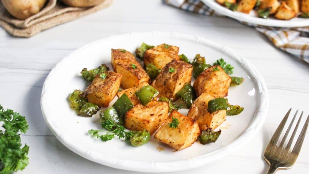Roasted potatoes with green bell peppers garnished with parsley on a white plate.