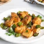 Roasted potatoes with green bell peppers garnished with parsley on a white plate.