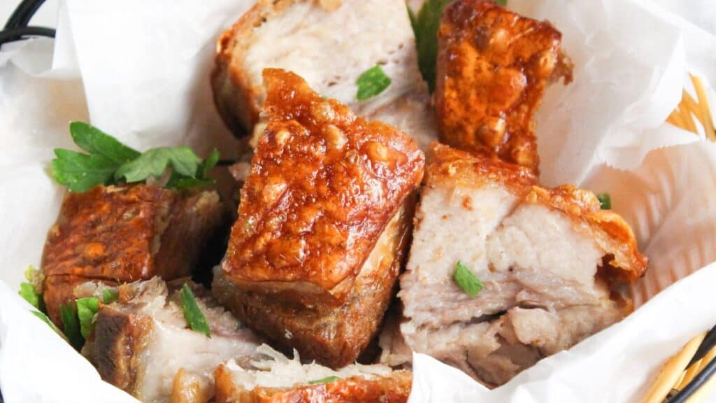 A basket of crispy pork belly pieces, garnished with parsley, served in a white paper-lined wicker basket.