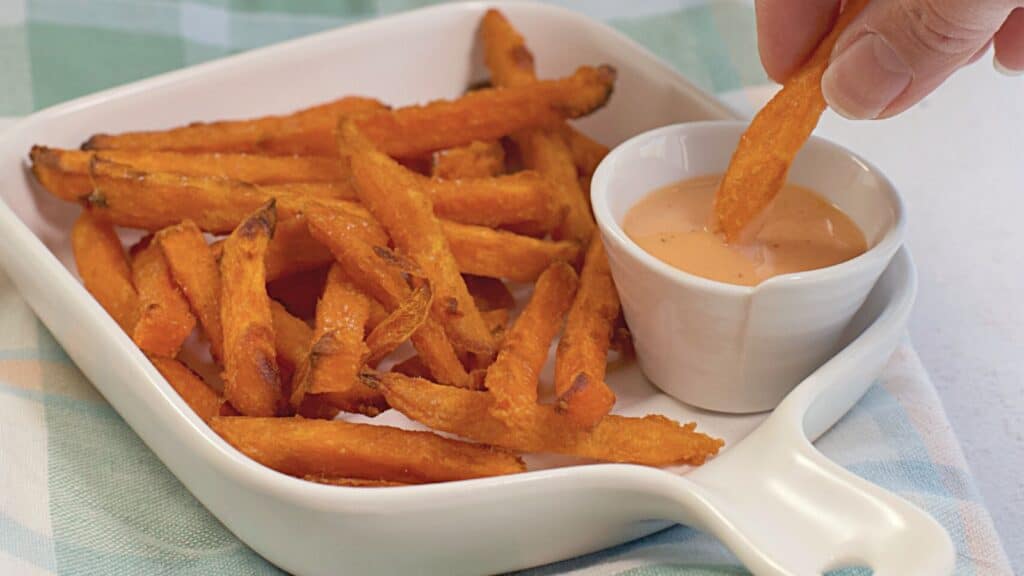 A serving of sweet potato fries with a side of dipping sauce.