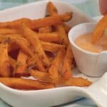 A serving of sweet potato fries with a side of dipping sauce.