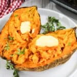 Two halves of a baked sweet potato topped with butter, garnished with thyme, on a white plate with a red checkered napkin.