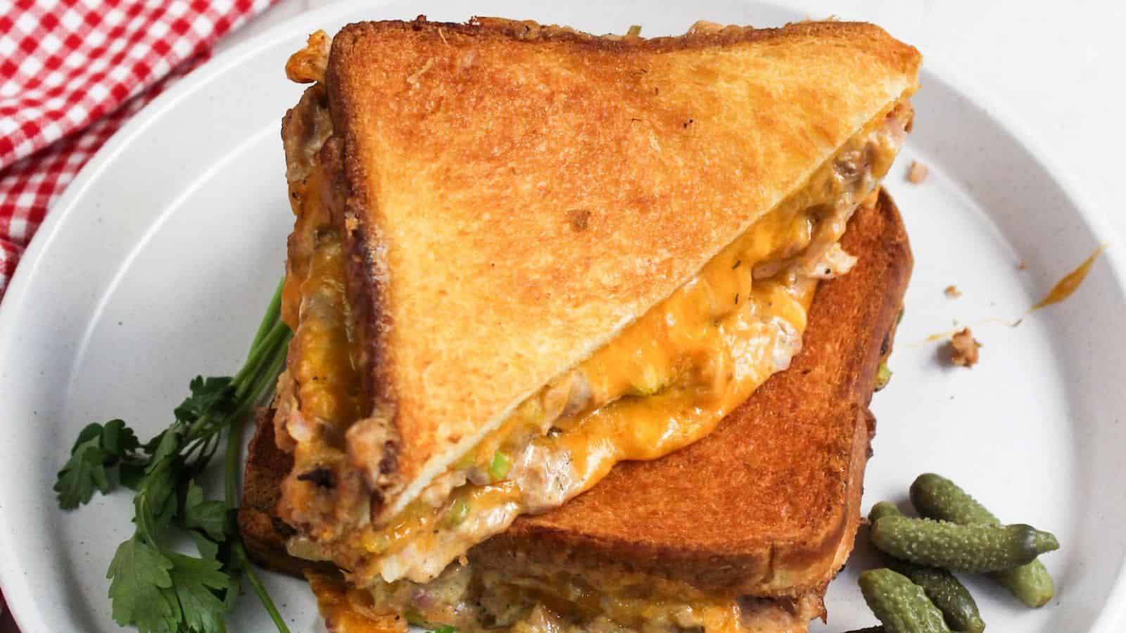 A grilled cheese tuna sandwich is cut in half on a plate.