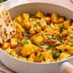 Vegetable curry served in a pan with a side of naan bread.