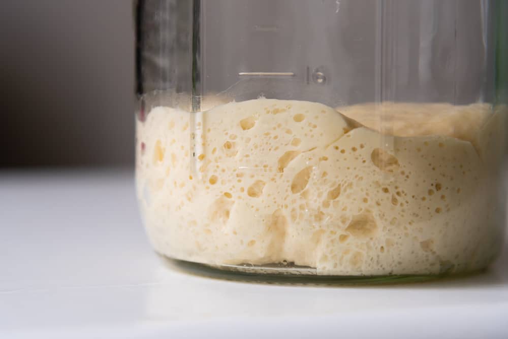 Active sourdough starter showing bubbles in a glass jar undergoing feeding.