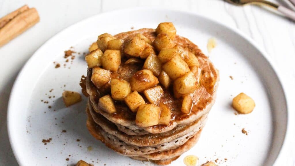 A stack of pancakes topped with cinnamon-spiced apples on a white plate.