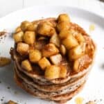 A stack of pancakes topped with cinnamon-spiced apples on a white plate.