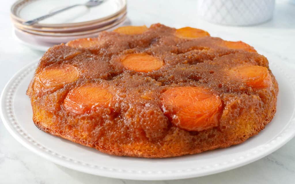 A peach upside-down cake on a white plate, with caramelized peaches visible on top, set on a marble countertop.