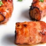 Three pieces of bacon-wrapped salmon bites garnished with parsley on a white plate.