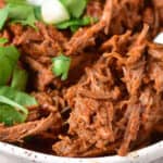 A bowl of pulled barbeque beef garnished with fresh herbs.