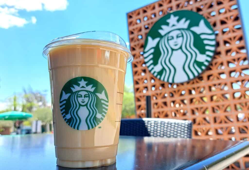 Iced coffee in a plastic cup with a Starbucks logo, set on a table with a larger Starbucks logo in the background, is among the best Starbucks coffee drinks.