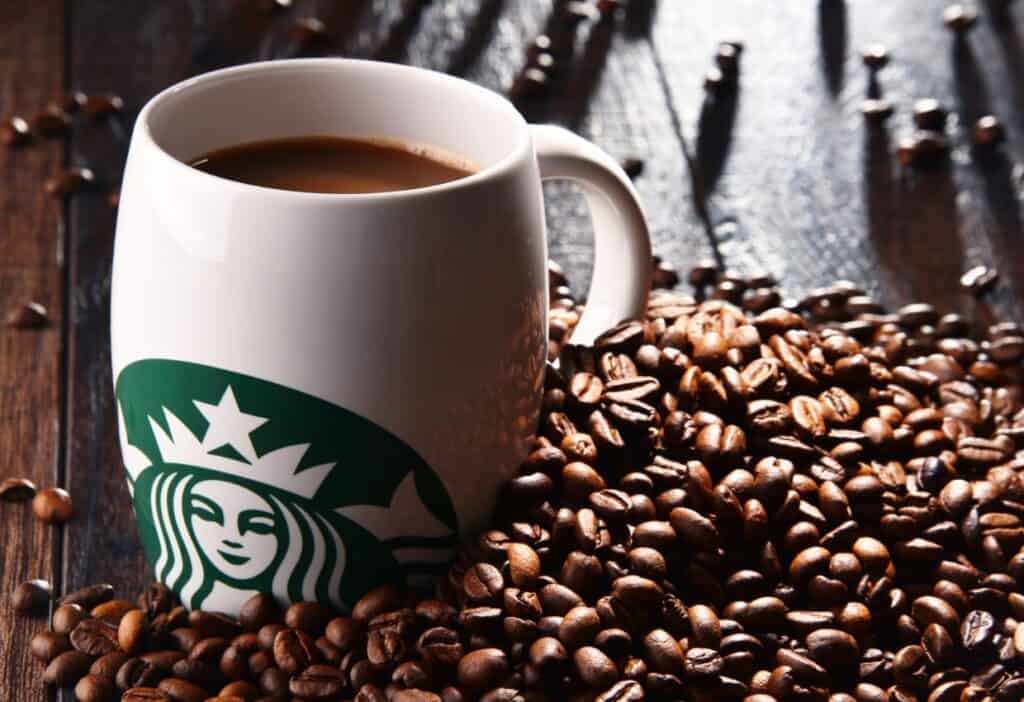 A Starbucks coffee cup surrounded by coffee beans on a wooden surface represents some of the best Starbucks coffee drinks.