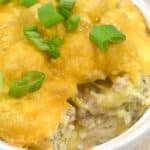 Cheesy casserole in a white dish topped with green onions, showing a serving spooned out to reveal layers inside.