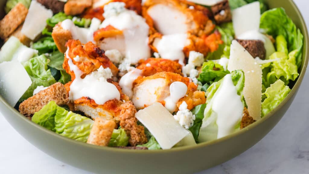 A fresh caesar salad with grilled chicken, croutons, parmesan cheese, and drizzled dressing in a green bowl.