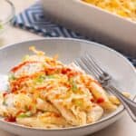 A plate of cheesy baked pasta and chicken casserole served with chopped scallions, accompanied by a baking dish and fork.