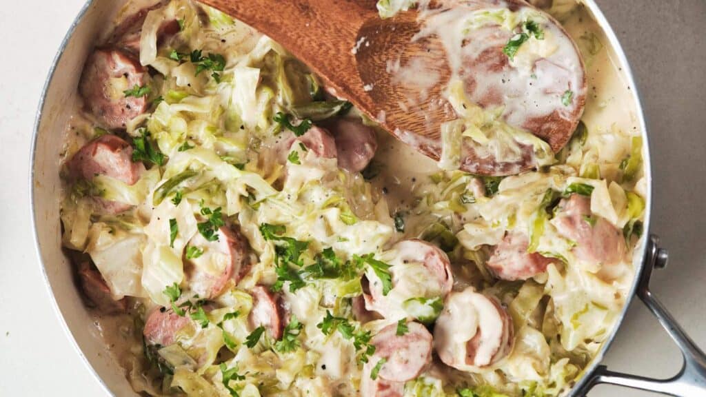 Creamy sausage and cabbage skillet dinner garnished with herbs in a pan.