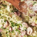 Creamy sausage and cabbage skillet dinner garnished with herbs in a pan.