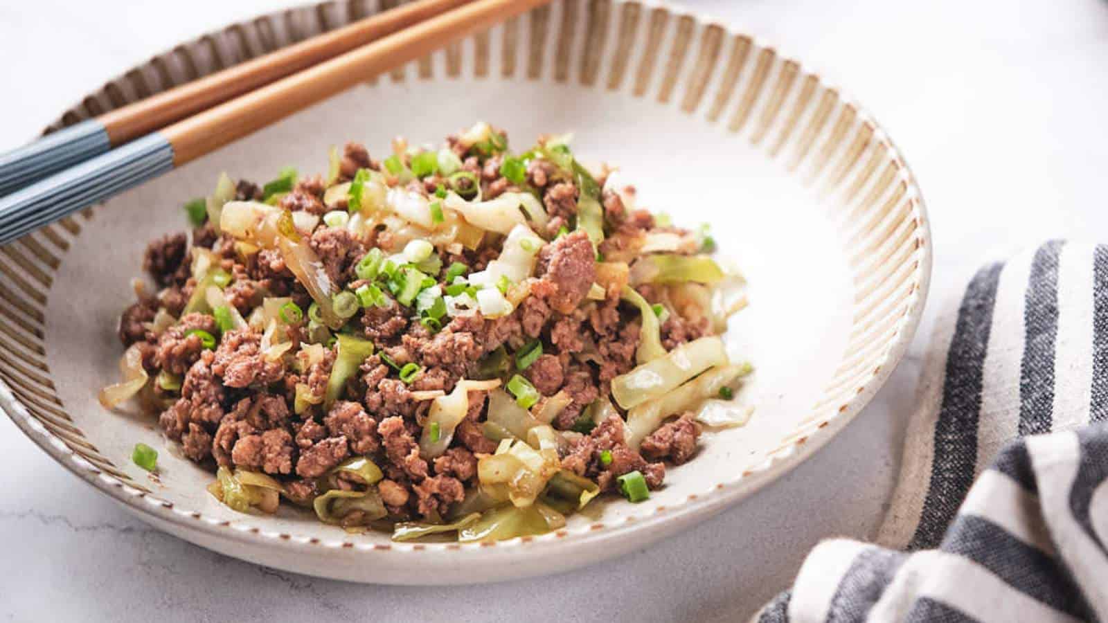 A plate of stir-fried minced meat with green onions, served with chopsticks on a marble countertop.