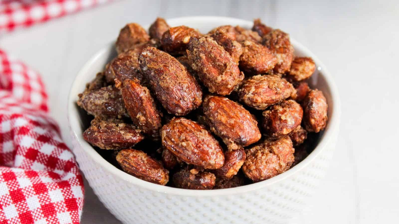 A bowl of candied almonds on a wooden table, with a red and white checkered napkin partially visible.