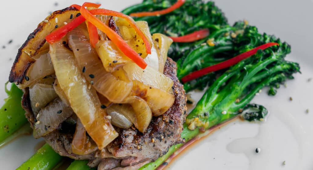 Grilled steak topped with caramelized onions, served with broccolini and a creamy sauce.