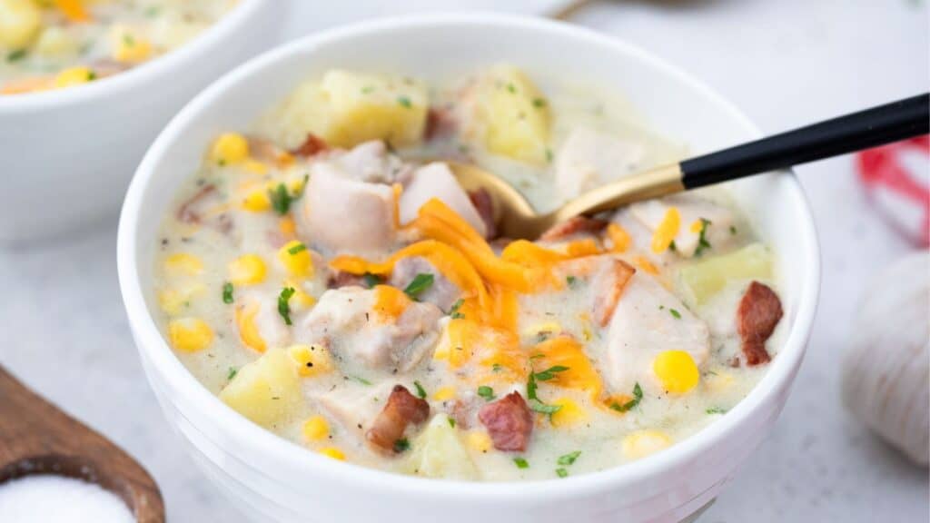 A bowl of creamy chicken corn chowder with potatoes and garnished with shredded cheese.