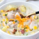 A bowl of creamy chicken corn chowder with potatoes and garnished with shredded cheese.