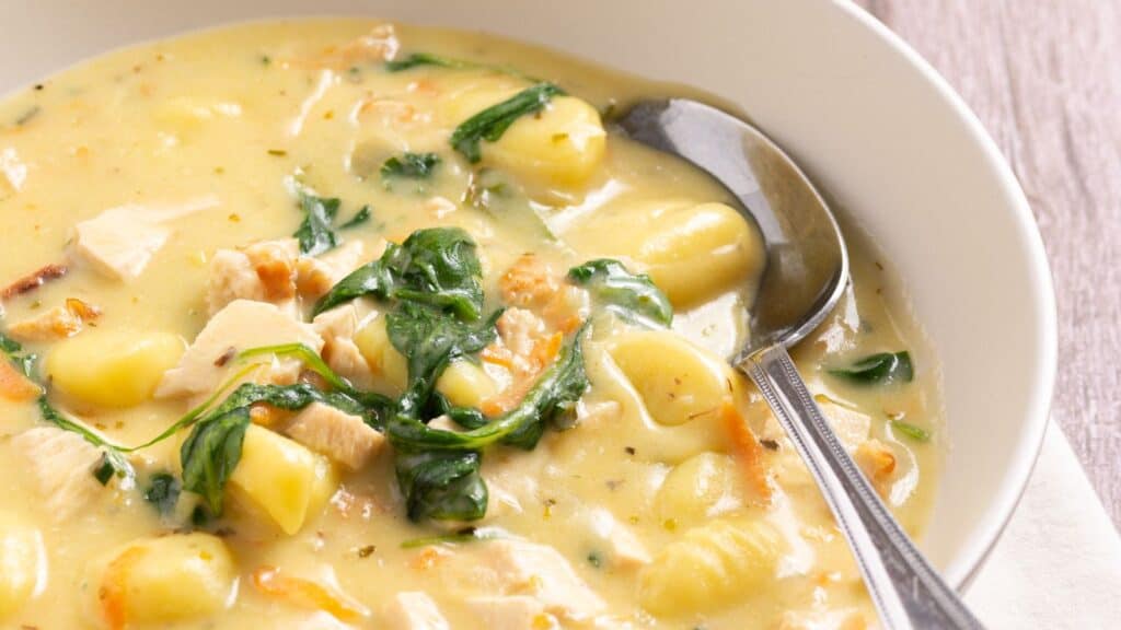 A bowl of creamy soup with gnocchi, spinach, and chunks of chicken.
