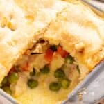 Homemade chicken pot pie with a flaky crust and a scoop removed, revealing the creamy filling with vegetables.