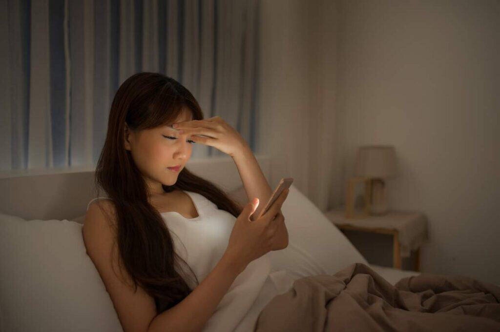 Woman browsing her smartphone in bed at night.