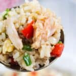 Close-up of a spoon holding fried rice with crab meat, green onions, and red bell peppers.