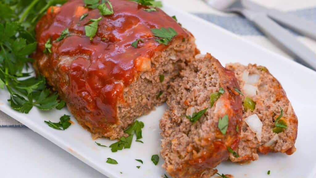 Sliced meatloaf on a white plate garnished with parsley.