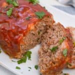 Sliced meatloaf on a white plate garnished with parsley.