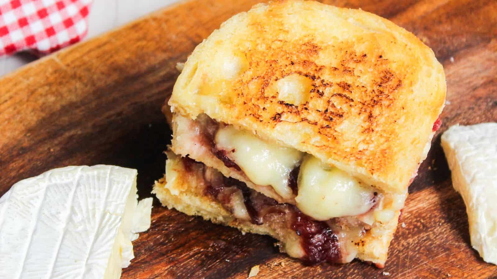 Grilled cheese sandwich with melted cheese and cranberry sauce on a wooden board.