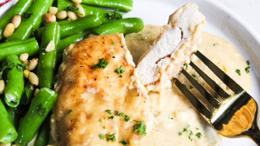A plate with chicken, green beans, and pine nuts served with a creamy sauce.
