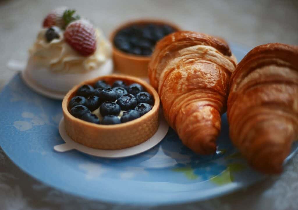 A plate with croissants and a bowl of blueberries, accompanied by a small dessert topped with a strawberry.
