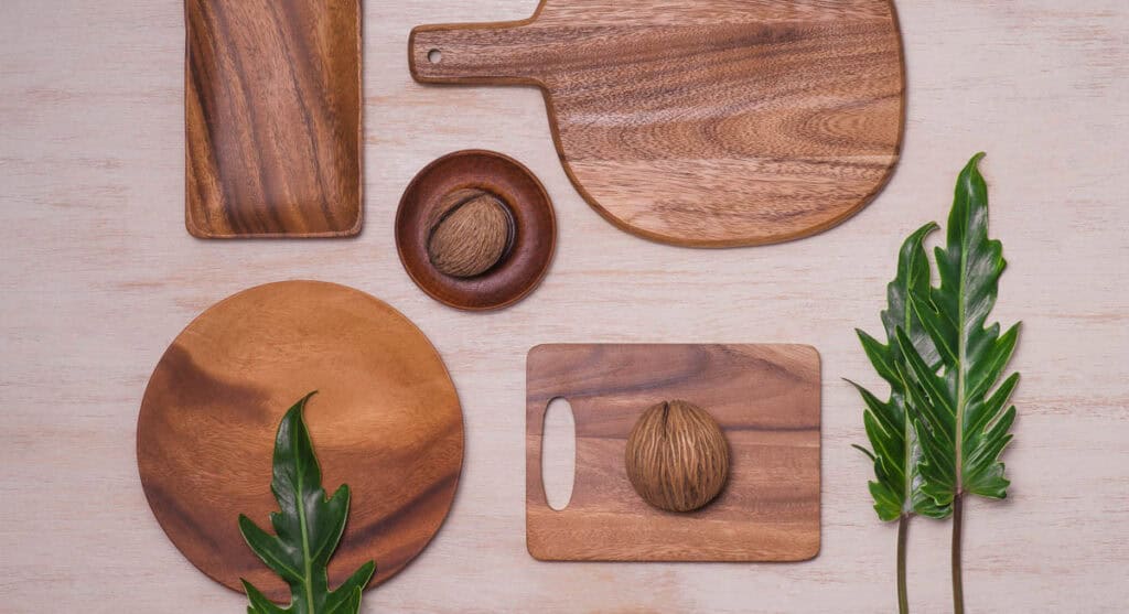 Various wooden kitchenware items and green leaves arranged on a light wooden surface.