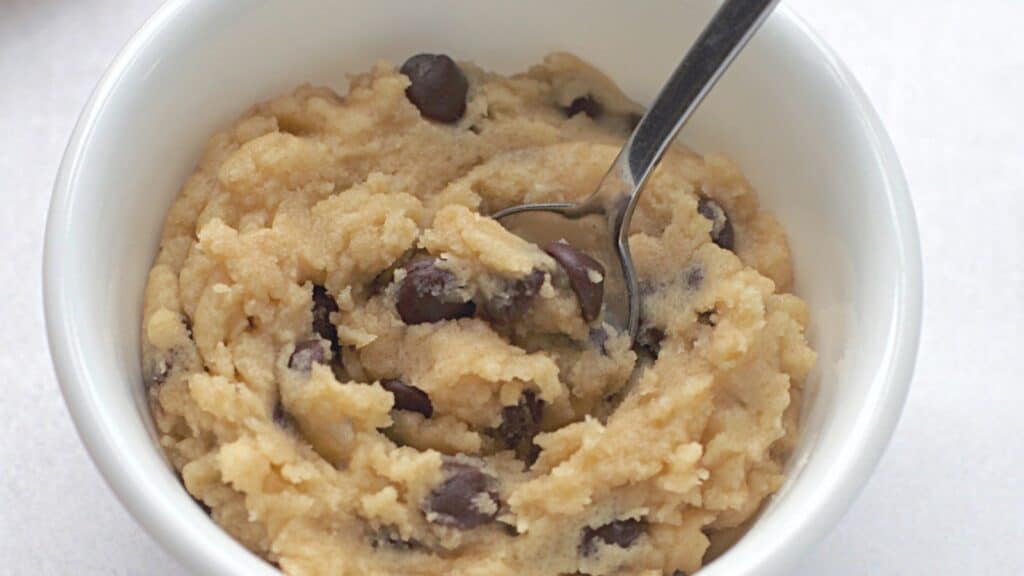 A bowl of cookie dough with chocolate chips and a spoon, on a white background.