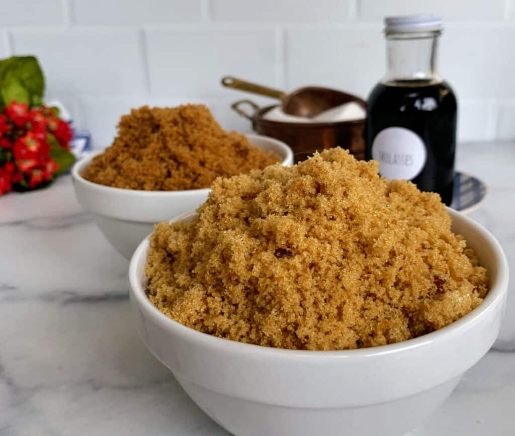 Bowls of brown sugar with a bottle of vanilla extract in the background on a kitchen counter.