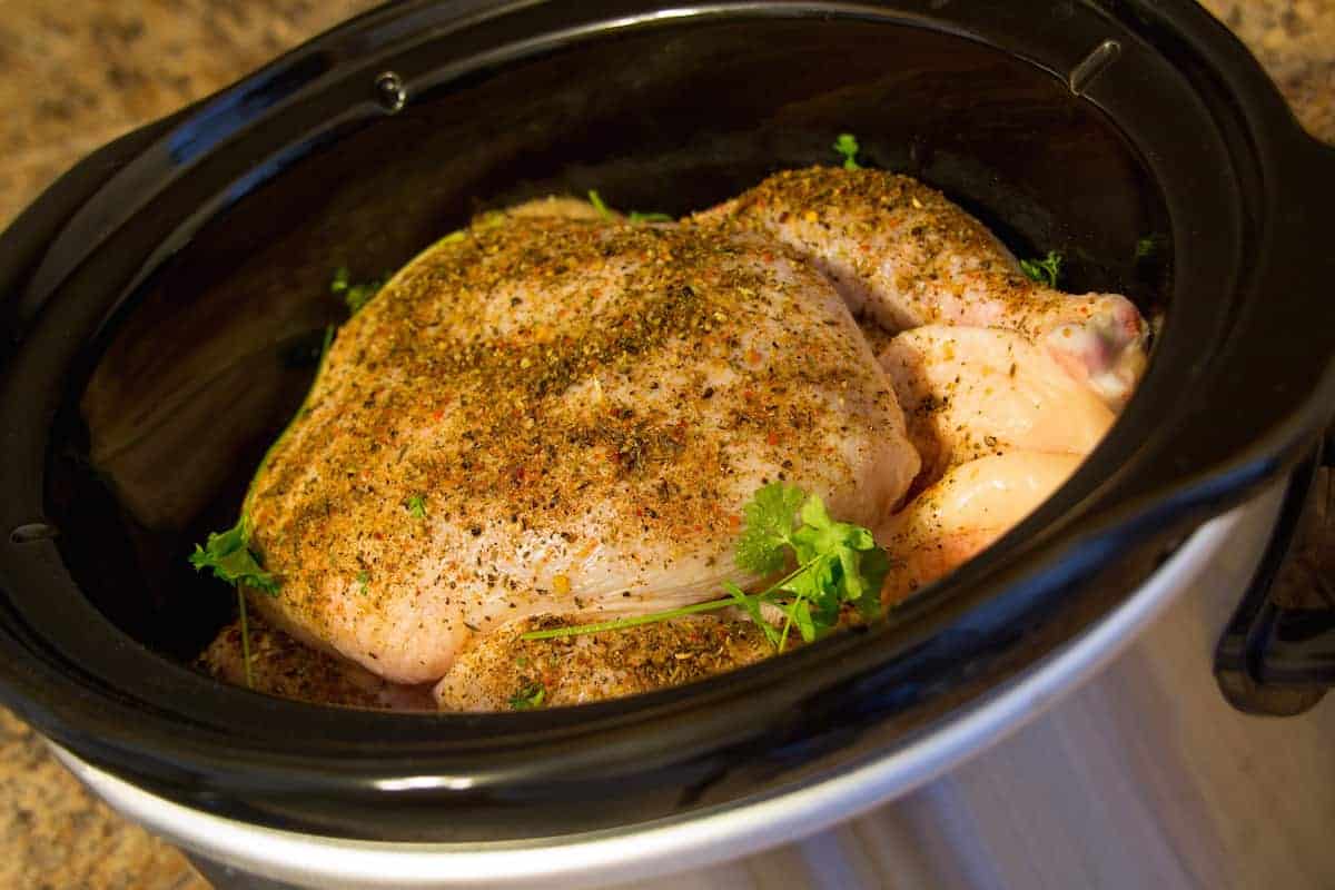 A whole chicken seasoned with herbs and spices in a slow cooker, ready to be cooked.